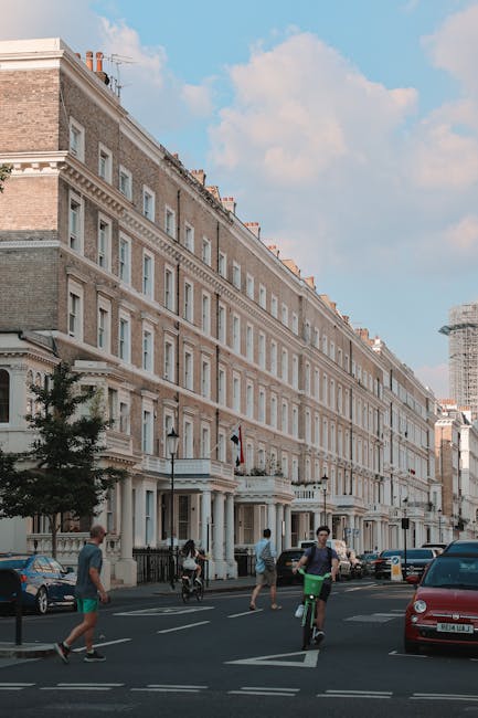 A street scene on Old Brompton Road featuring a line of multi-storey residential buildings with a mix of red brick, beige, and yellow facades, and large windows. A grey removal van belonging to Man Wi